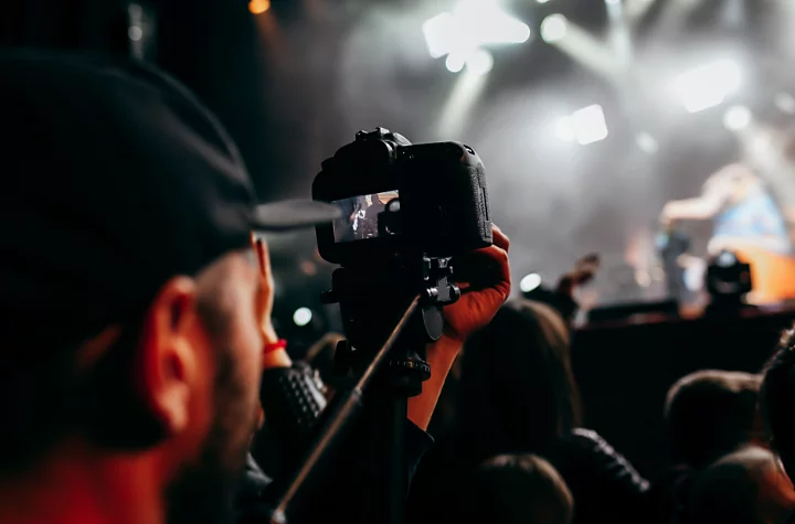 A photographer holding a camera on a tripod taking a photo of a band performing at a concert