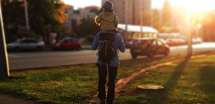 Child riding on father's shoulders through a park at sunset.