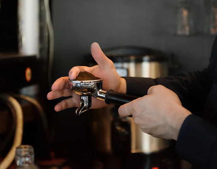 Een hand die een overvolle filterdrager met gemalen koffie van een koffiemachine vasthoudt