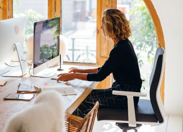 Sentada em uma cadeira, mulher digita em um computador.