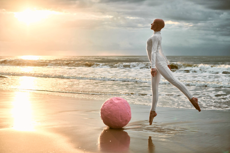 A person in white jumpsuit on a beach with a pink ball Description automatically generated