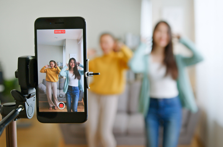 Making a TikTok dance Two young women record themselves dancing via a mobile phone that is held by a tripod.