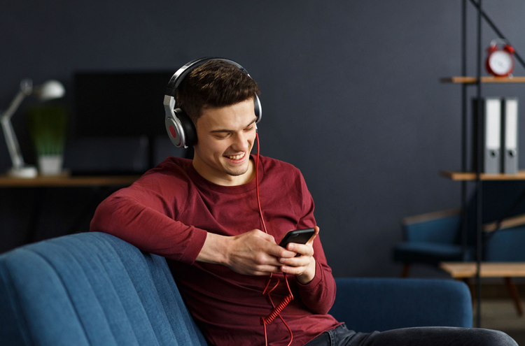 A person sitting on a coach with headphones plugged into their phone listening to music from YouTube's Audio Library