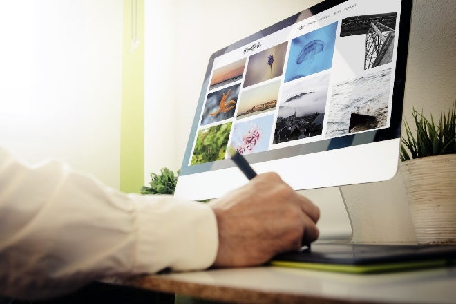 A person taking notes on a tablet with a view of a design portfolio on a desktop