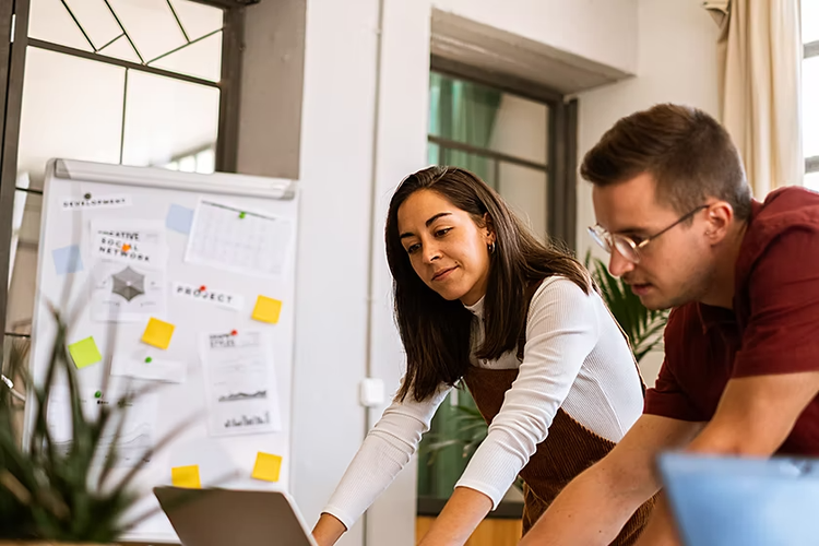 Two people standing and staring down at a laptop together to create an annual report