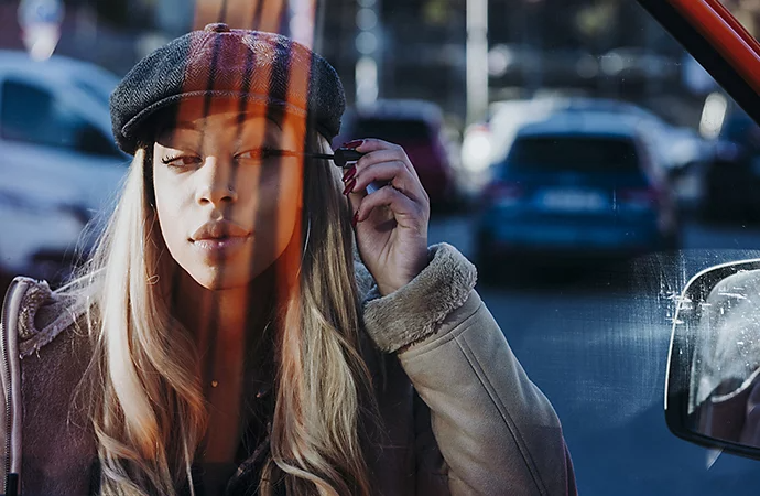 Candid photo of the relflection in a car window of a woman applying mascara