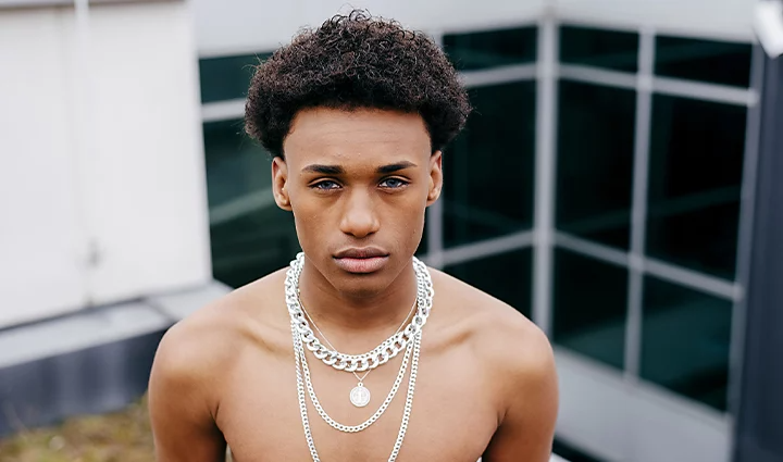 A person staring into a camera wearing chain necklaces