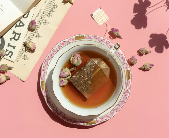 An artistic flat lay photo of a few flowers in a teacup filled with tea and surrounded by decorations