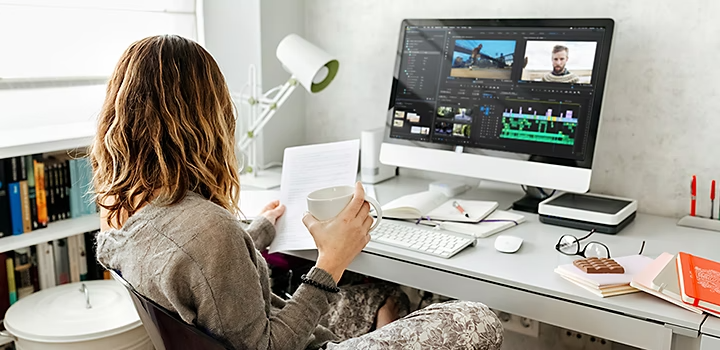 A video editor editing a video in Adobe Premiere Pro while reviewing production notes