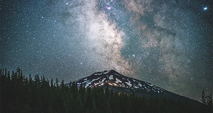 A snow-covered mountain with a starry night sky behind it