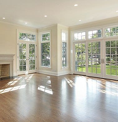 An interior photo of an empty room with large windows and a hardwood floor.