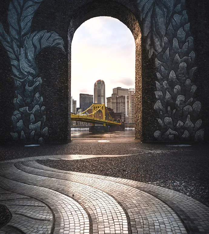 Photo of a bridge connecting to a city seen through a door arch