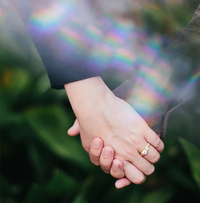 A prism reflecting a rainbow onto the hands of people who are holding hands together