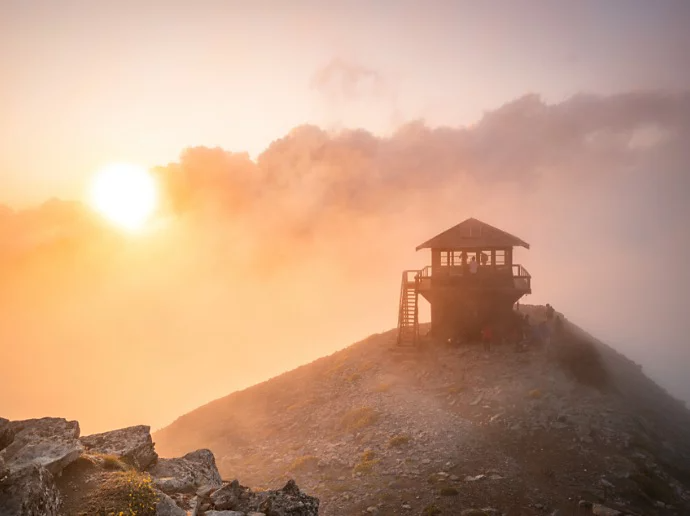 The sun peeking through clouds and illuminating a lifeguard hut on the shore