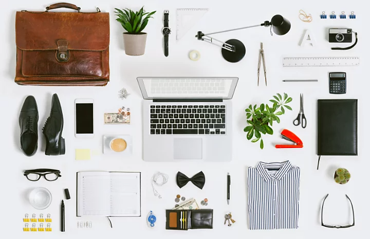 A flat lay photo of numerous pieces of office equipment and dress around a laptop computer