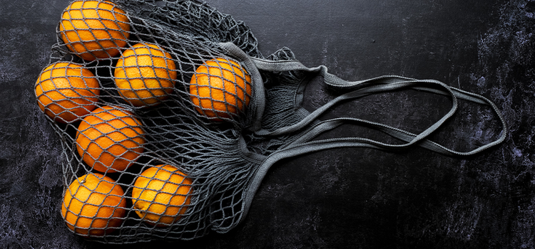 A black mesh bag filled with a few oranges resting on a black background