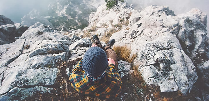 Scatto aereo di un escursionista seduto in cima a una montagna che si affaccia sulle nuvole in un video promozionale