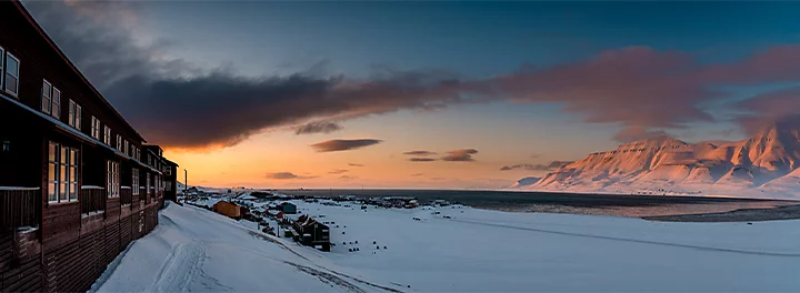 Wide angle photo of a resort overlooking a body of water in front of snowy mountains