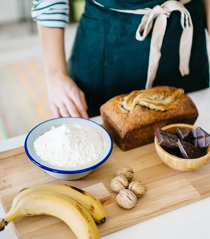 Bizcocho de plátano sobre una tabla de cortar junto a los ingredientes empleados para cocinarlo