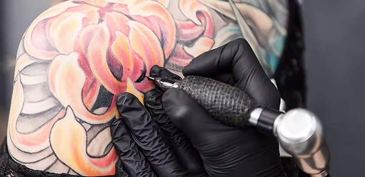 Artista de tatuaje aplica color de relleno a un diseño de tatuaje