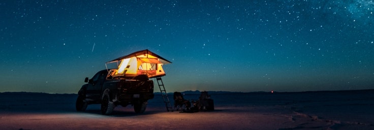 A pickup truck and tent under a starry sky at night