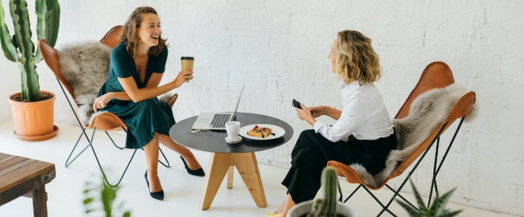 Two seated women having conversation across from each other at a small round table