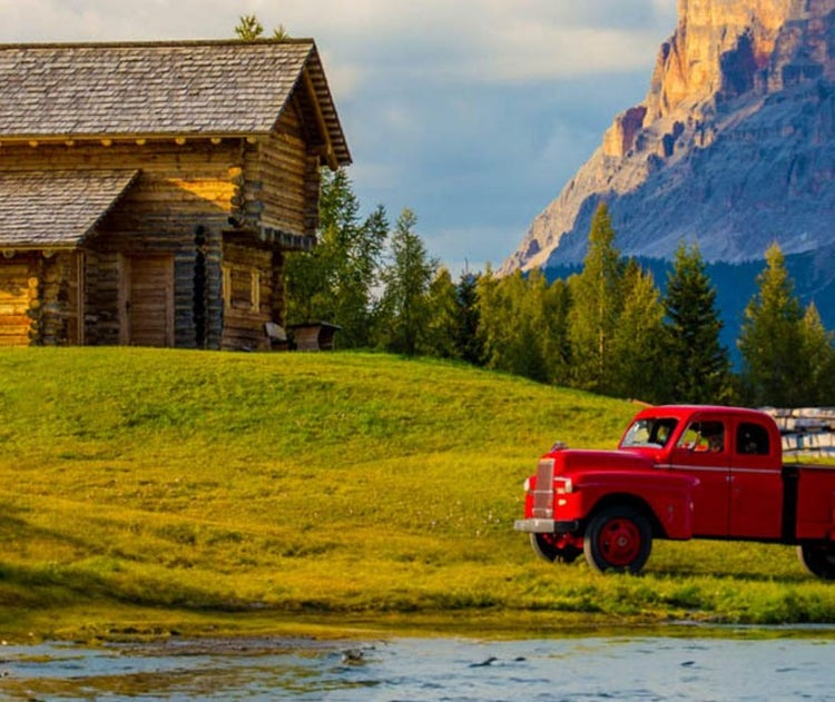 A red truck in a field with a cabin and mountain in the background
