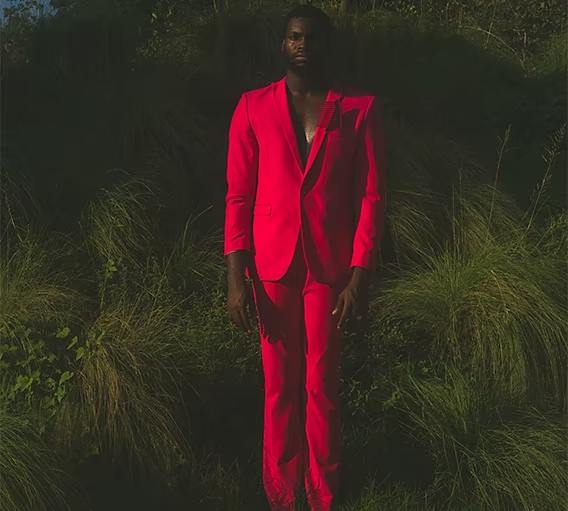 A person standing in front of various tall plants while wearing a bright red suit