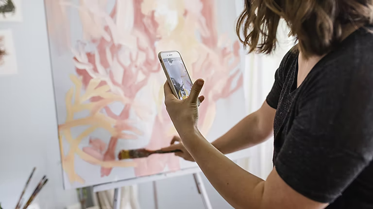 Person using their mobile phone to record a video of themselves making a painting