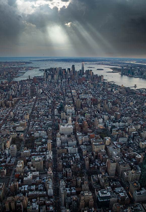 Beams of light struggling to shine through thick clouds in a bird's-eye cityscape image of Manhattan