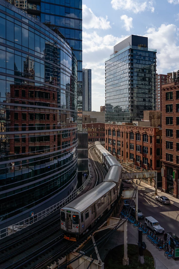 A subway train moving along its curved raised track around a building in a cityscape