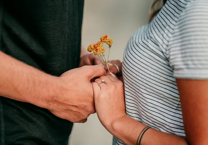 A close-up engagement photo of a couple holding hands.