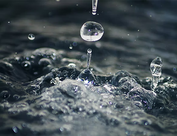 A close-up photo of a rain droplet landing in a puddle of water.