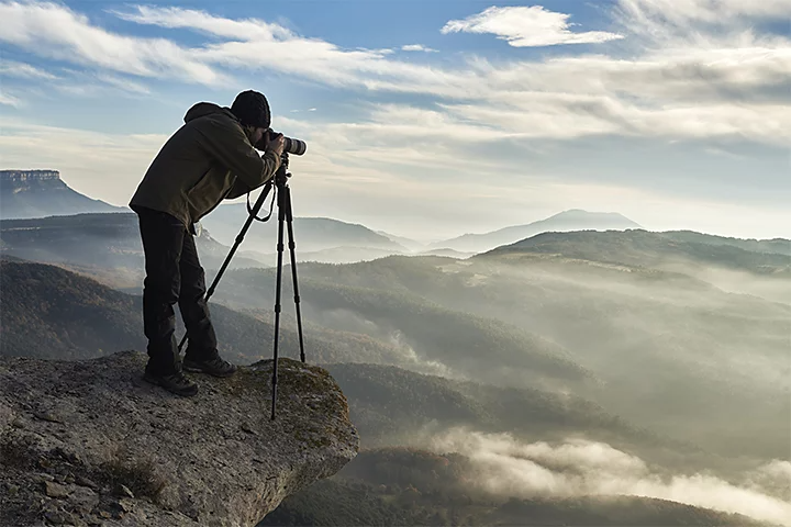 A photographer taking a photo from a cliff using a camera on a tripod with a telephoto lens