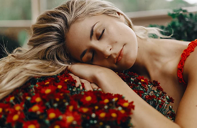 A model posing by laying their head on a planter of flowers