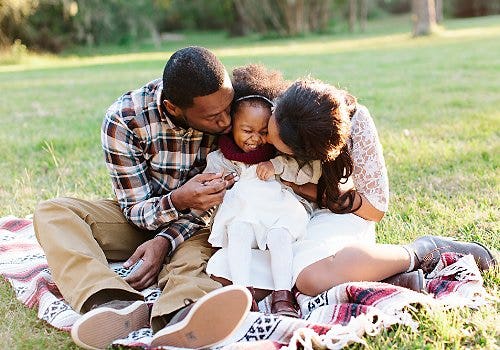 A photo of a family cuddling on a blanket at a park.