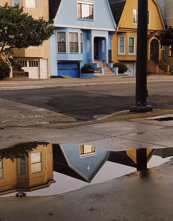 Colorful townhomes reflected in a large puddle of water on a sidewalk