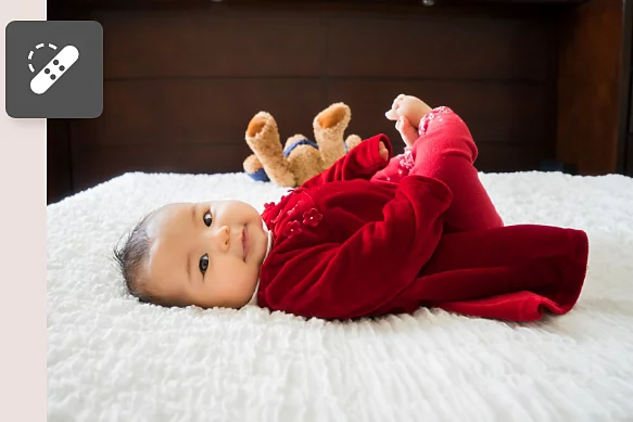 A photo of a newborn baby lying on a bed with a stuffed animal in the background.