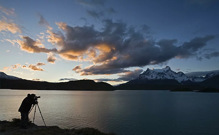 A photographer setting up their camera on a tripod next to a lake