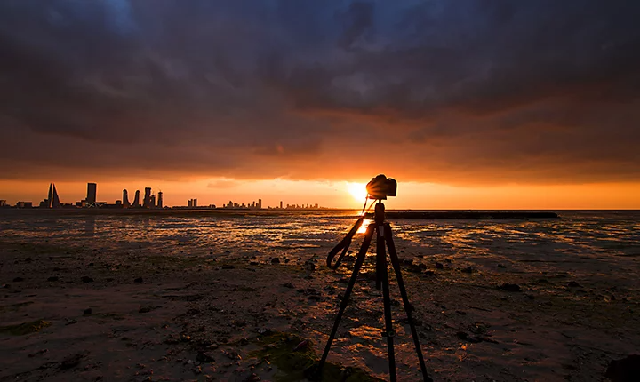 A camera on a tripod with a sunrise and cityscape in the background