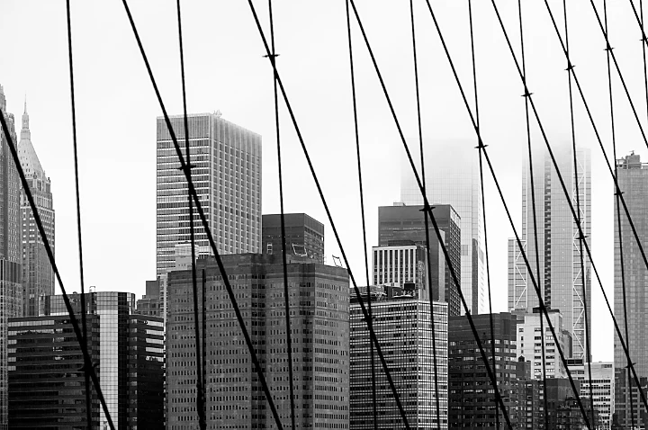 A black-and-white cityscape as captured through the string-like supports of a city bridge