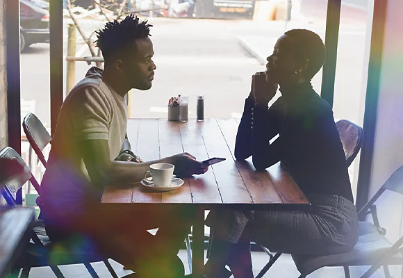 The image of two people in conversation at a coffee shop obscured by a rainbow lens flare