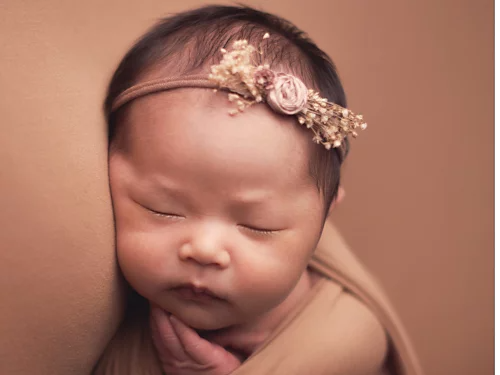 A photo of a sleeping newborn baby with a headband on their head.