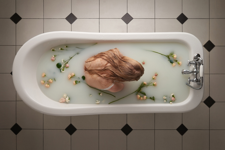 A photo of a person sitting in a milk bath, taken from the ceiling looking down.