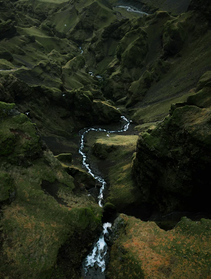 The rushing white water of a stream splitting a lush green valley in half as captured from above