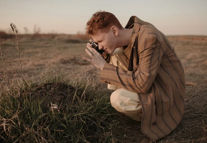 A scientist photographing a large dirt mound among tall grass in a field