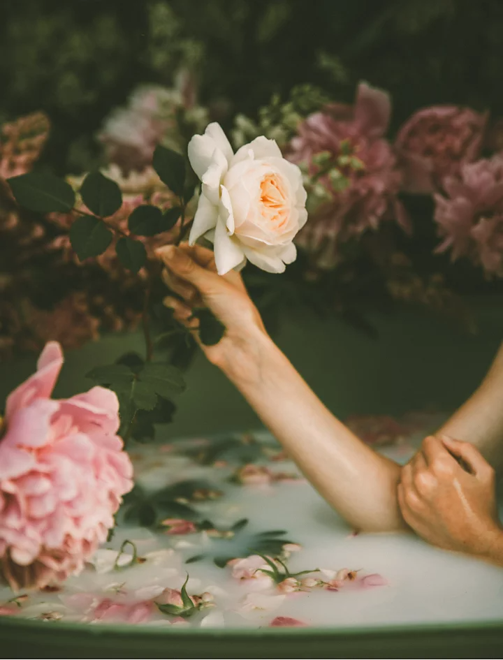 A photo of a person sitting in a milk bath holding a flower.