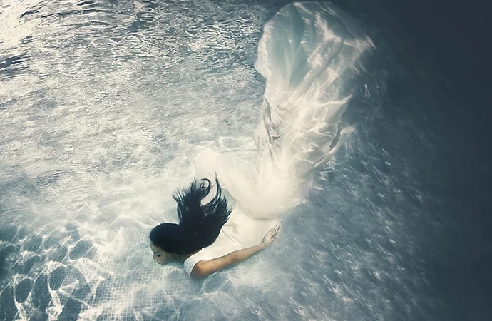 An underwater photo of a person who just dived head first into a pool while wearing a dress