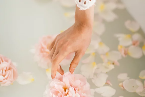 A photo of hand reaching for flowers in a milk bath.