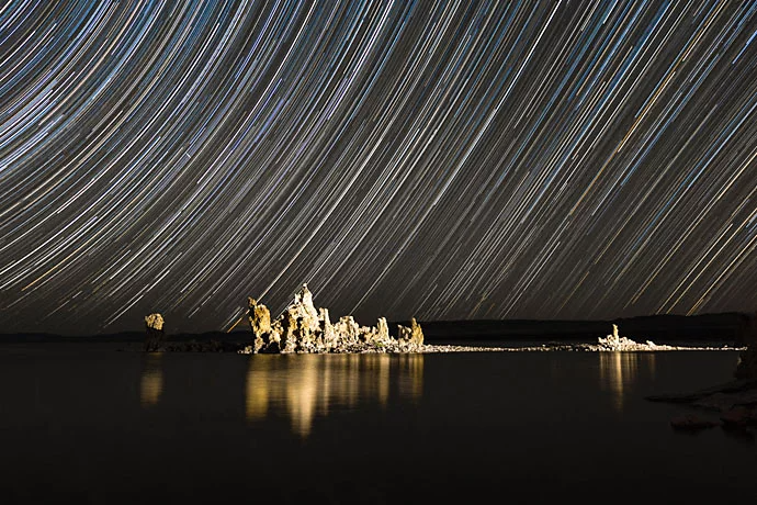 Star trails behind a small rock formation in a body of water